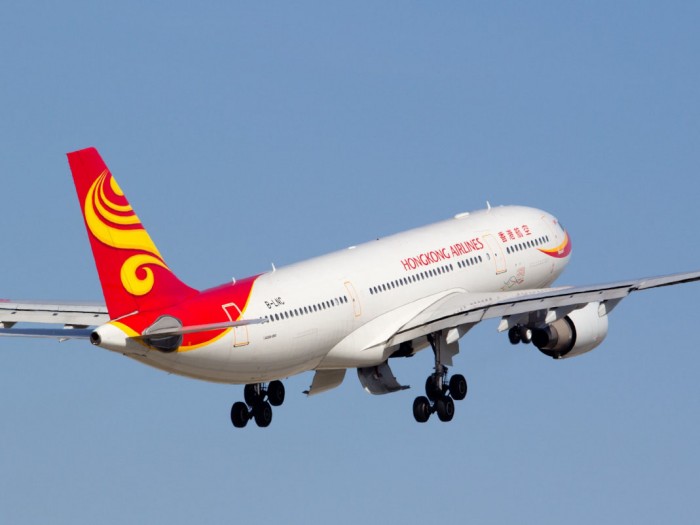A Hong Kong Airlines airplane after taking off but with its landing gear yet to be raised, set against a hazy blue sky
